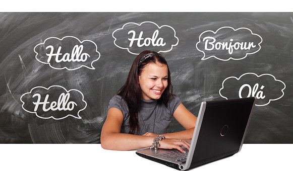 girl on computer; chalkboard says hello, hallo, hola, bonjour, ola