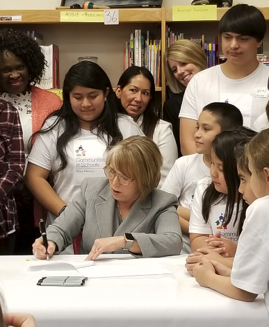 New Mexico students, teachers and legislators surround Governor Michelle Lujan Grisham as she signs a bill into law